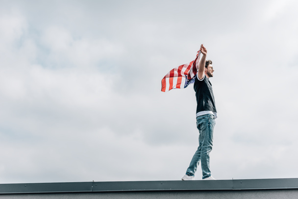 vista lateral de homem bonito em jeans e t-shirt segurando bandeira americana
  - Foto, Imagem