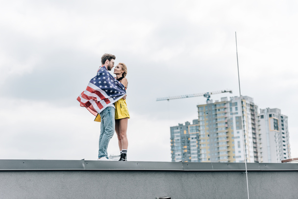 ελκυστική γυναίκα και όμορφος άντρας με αμερικάνικη σημαία αγκαλιάζοντας στη στέγη  - Φωτογραφία, εικόνα