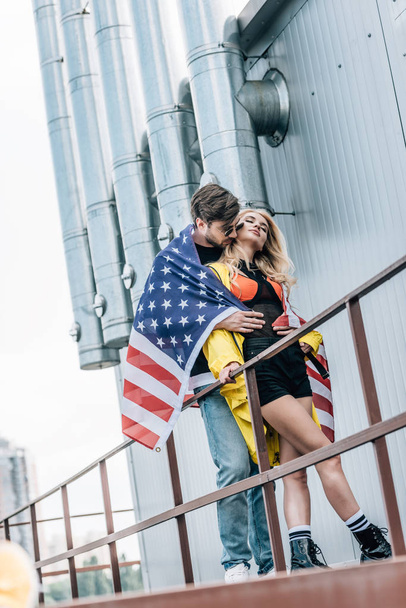 屋根の上に抱きしめるアメリカの旗を持つ魅力的な女性とハンサムな男  - 写真・画像