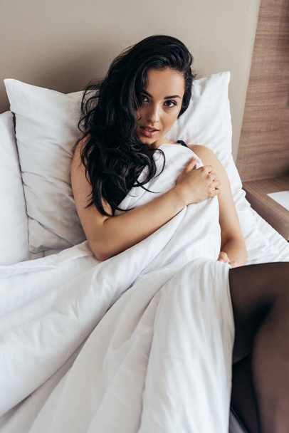 sensual brunette young woman in black stockings lying under blanket on bed - Photo, Image
