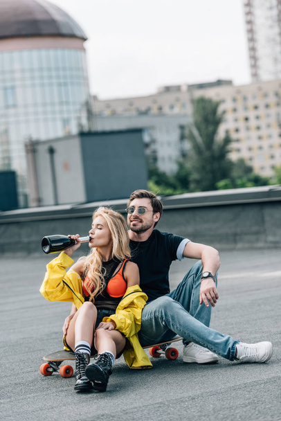 attractive woman drinking champagne and handsome man in glasses sitting on skateboard  - Fotografie, Obrázek