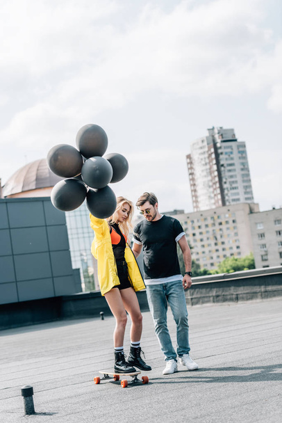 attractive woman with balloons skateboarding and man in glasses standing with her  - Fotografie, Obrázek