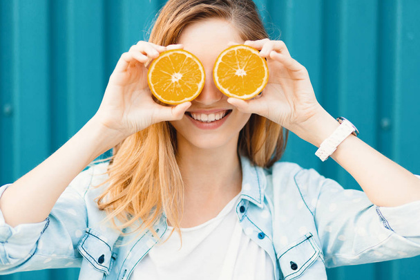 Carefree young beautiful girl using two halfs on oranges instead of glasses over her eyes - Zdjęcie, obraz