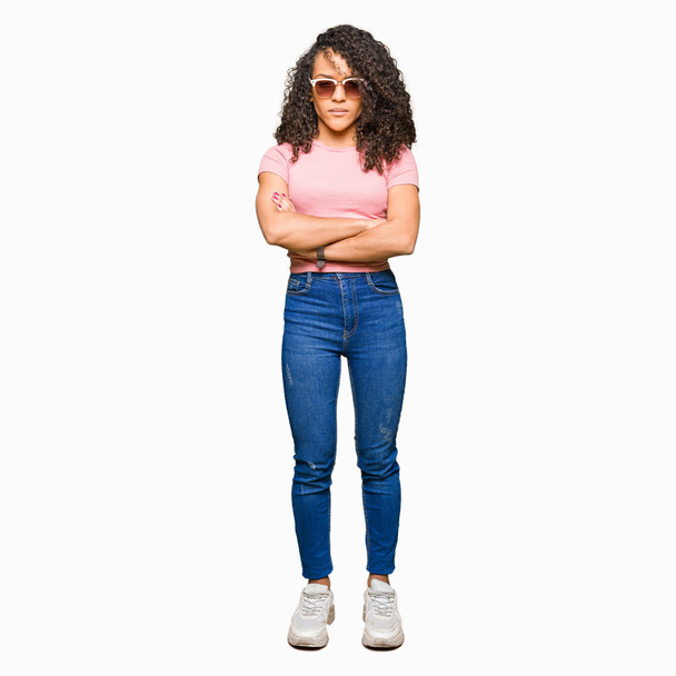 Young beautiful woman with curly hair wearing pink sunglasses skeptic and nervous, disapproving expression on face with crossed arms. Negative person. - Photo, image