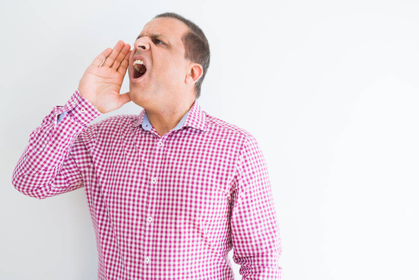 Mężczyzna w średnim wieku nosić koszulę biznesową nad białą ścianę krzycząc i krzyczeć głośno na bok z ręką na ustach. Koncepcja komunikacji. - Zdjęcie, obraz