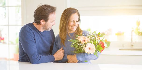Couple romantique d'âge moyen tenant des fleurs en amour à la maison
 - Photo, image