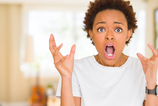 Jonge mooie Afrikaanse Amerikaanse vrouw het dragen van casual wit t-shirt gek en boos schreeuwen en schreeuwen met agressieve expressie en armen verhoogd. Frustratie concept. - Foto, afbeelding