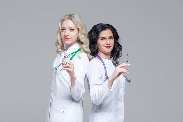 Two female doctors standing back-to-back hold ready-to-inject syringes - Photo, Image