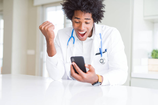クリニックでスマートフォンを使用して、誇らしげに叫び、勝利と成功を祝うアフリカ系アメリカ人の医師の男性は、非常に興奮し、感情を応援 - 写真・画像