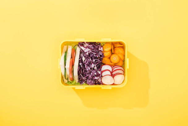 top view of lunch box with sandwiches and vegetables on yellow background - Photo, Image