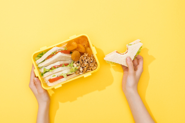 cropped view of lunch box with nuts, dried apricots and sandwiches in woman hands - Photo, Image