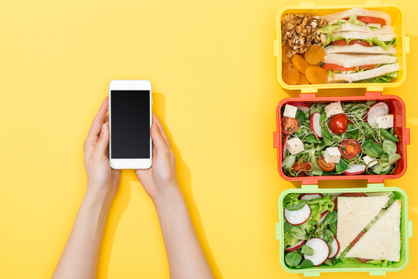 cropped view of woman holding smartphone near lunch boxes with food - Photo, Image
