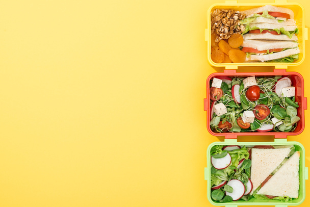 ylhäältä näkymä kolmesta lounaslaatikosta, joissa on ruokaa keltaisella taustalla
 - Valokuva, kuva