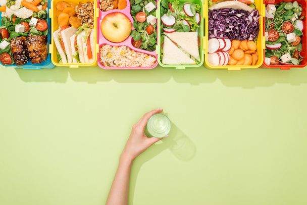 cropped view of woman holding glass of water in hand near lunch boxes with food - Photo, Image