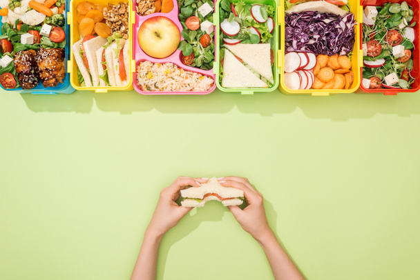 oříznutý pohled na ženu držící sendvič v ruce blízko polední krabice s jídlem - Fotografie, Obrázek