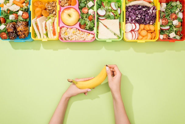 cropped view of woman holding banana in hands near lunch boxes with food - Photo, Image