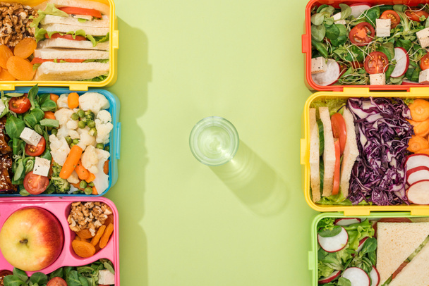 top view of lunch boxes with food near glass of water - Photo, Image