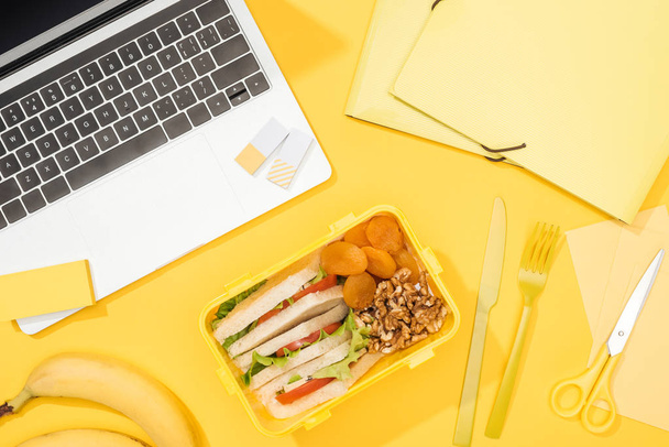 Draufsicht auf Lunchbox mit Lebensmitteln in der Nähe von Laptop und Bürobedarf - Foto, Bild