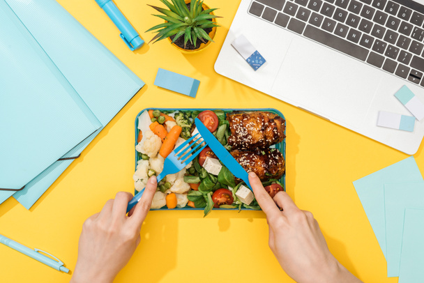 cropped view of woman holding fork over lunch box with food near laptop and office supplies - Photo, Image