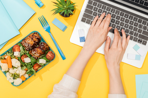przycięte widok kobiety pracujących z laptopem w pobliżu pudełka na lunch i materiałów biurowych - Zdjęcie, obraz