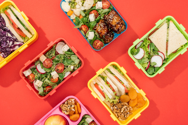 top view of lunch boxes with food on bright red background - Foto, imagen