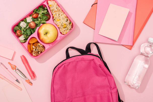 top view of backpack, lunch box with food and stationery on pink background - Photo, Image