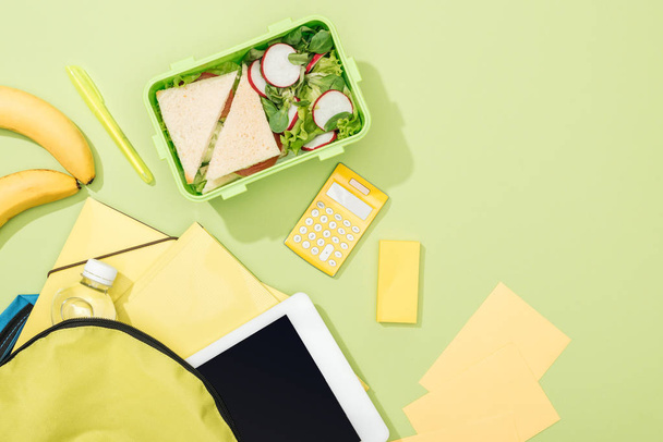 top view of lunch box with sandwiches and salad near backpack with stationery - Photo, Image
