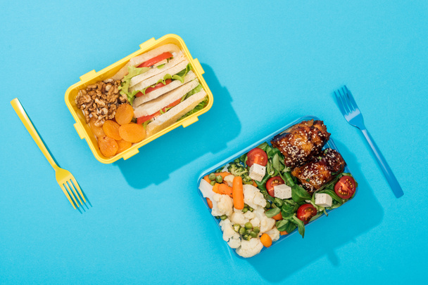 top view of plastic forks near lunch boxes with food on blue background - Photo, Image