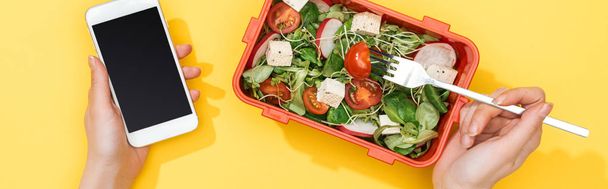 cropped view of woman holding smartphone and fork in hands near lunch box with salad - Фото, зображення