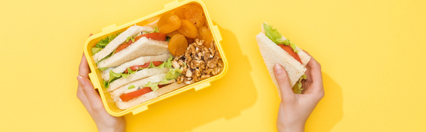 обрізаний вид жінки, що тримає сендвіч та обідню коробку з їжею в руках
 - Фото, зображення