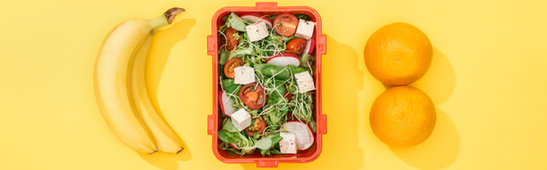 Panoramaaufnahme einer Lunchbox mit Lebensmitteln in der Nähe von Bananen und Orangen - Foto, Bild