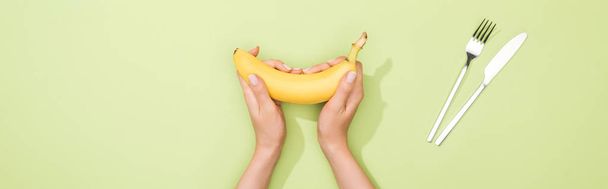 cropped view of woman holding banana in hands near fork and knife - Photo, Image