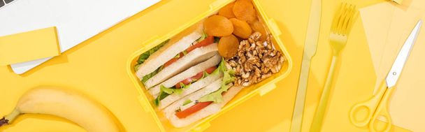 panoramic shot of lunch box with food near banana, knife and fork - Photo, Image