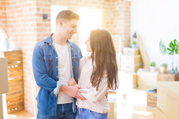 Beautiful young couple moving to a new home, standing on new aparment around cardboard boxes, hugging smiling happy and in love - Foto, immagini