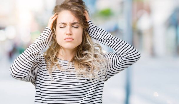 Beautiful young blonde woman wearing stripes sweater over isolated background with hand on head for pain in head because stress. Suffering migraine. - Photo, Image