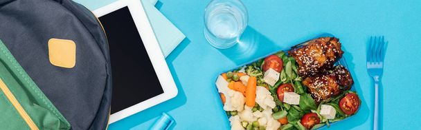 colpo panoramico di zaino con cartelle, tablet digitale, cancelleria vicino al bicchiere d'acqua e scatola per il pranzo
 - Foto, immagini