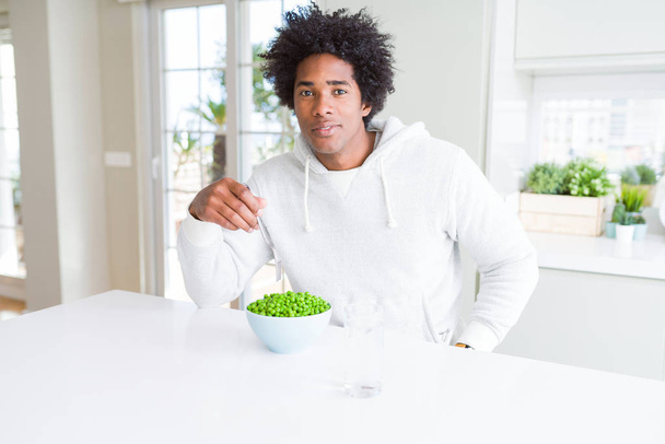 Hombre afroamericano comiendo guisantes verdes frescos en casa con una expresión segura en la cara inteligente pensando en serio
 - Foto, Imagen