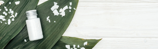 vue du dessus du produit de beauté de noix de coco en bouteille sur des feuilles de palmier vert avec des flocons de noix de coco sur une surface en bois blanc avec espace de copie, vue panoramique
 - Photo, image