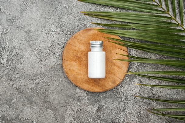 top view of coconut beauty product in bottle on wooden board near palm leaf on grey textured background - Photo, Image