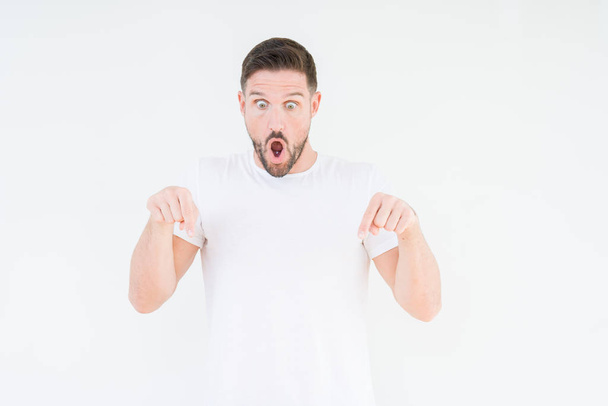 Молодой красивый мужчина в обычной белой футболке на изолированном фоне указывает вниз пальцами показывая рекламу, удивленное лицо и открытый рот
 - Фото, изображение