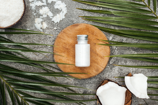 灰色のテクスチャーの背景にヤシの葉の近くの木製のボード上のボトルのココナッツの美しさの製品のトップビュー - 写真・画像