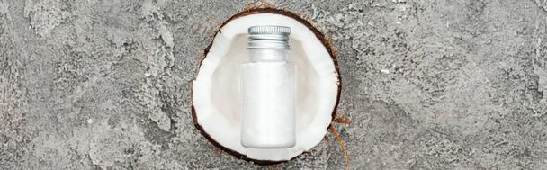 вид сверху на крем в бутылке на половину кокоса на сером текстурированном фоне, панорамный снимок
 - Фото, изображение