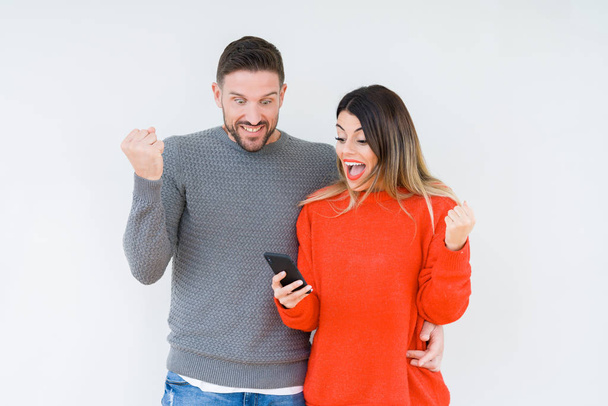 Young couple using smartphone over isolated background screaming proud and celebrating victory and success very excited, cheering emotion - Фото, изображение