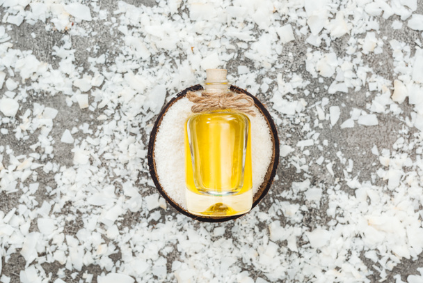 pohled na olej v láhvi na kokosu napůl na šedém pozadí s kokosovými hoblaky - Fotografie, Obrázek