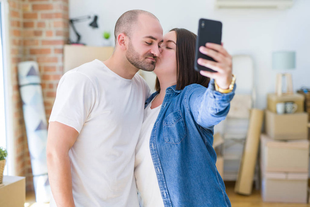 Young couple taking a picture photo using smartphone at new home, smiling happy for moving to new apartment - 写真・画像