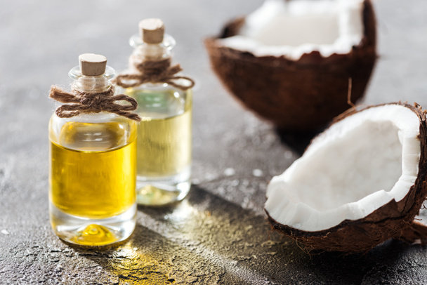selective focus of bottles with coconut oil near coconut halves on grey background - Foto, immagini