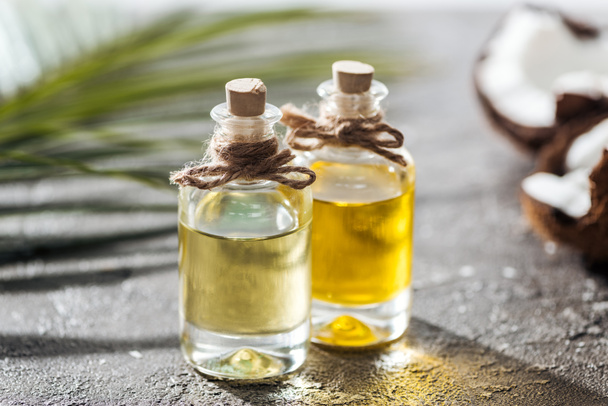 selective focus of bottles with coconut oil near green palm leaf and cracked coconut - Foto, Imagem