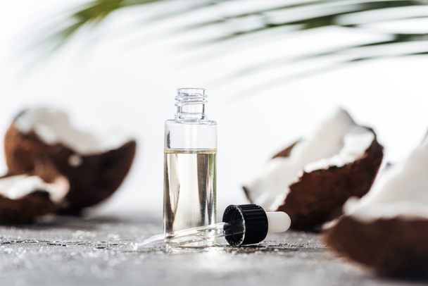selective focus of open bottle with coconut serum near dropper and cracked coconuts - 写真・画像