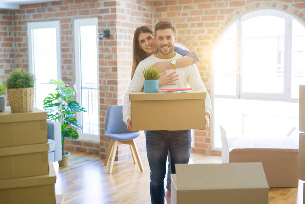 Belo jovem casal se mudando para uma nova casa, sorrindo feliz segurando caixas de papelão no novo apartamento
 - Foto, Imagem