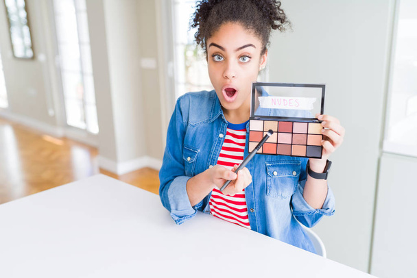 Young african american woman holding shadows cosmetics palette scared in shock with a surprise face, afraid and excited with fear expression - Фото, зображення